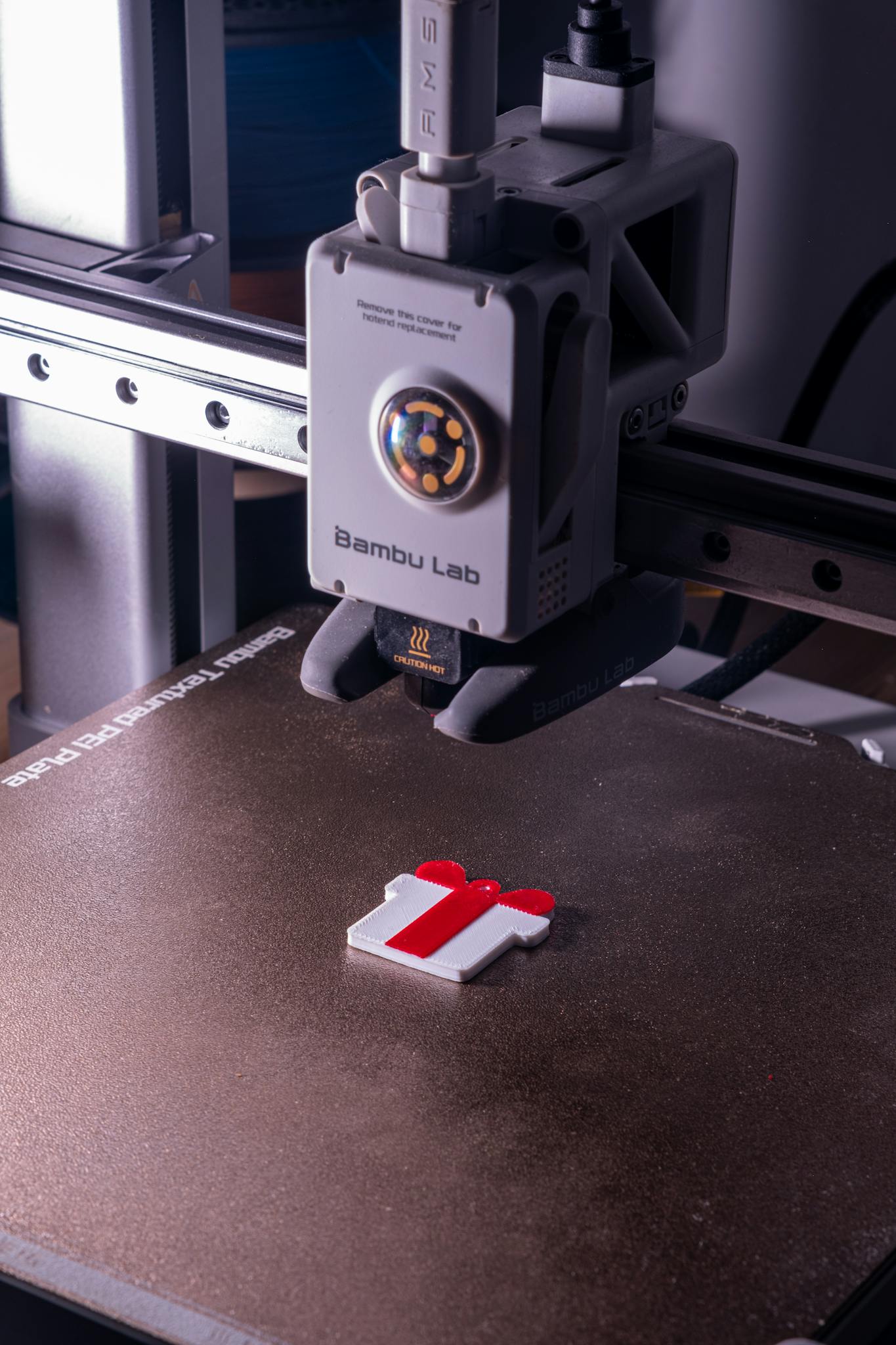 Close-up of a 3D printer fabricating a red and white object on a build plate.