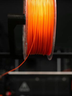 Close-up of an orange 3D printer filament spool in a workshop setting, highlighting innovation and design.