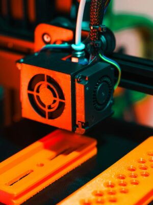 Detailed view of a 3D printer in action, extruding orange plastic components.