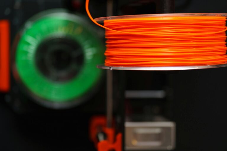 Detailed view of orange and green 3D printer filament spools, perfect for creative and industrial projects.
