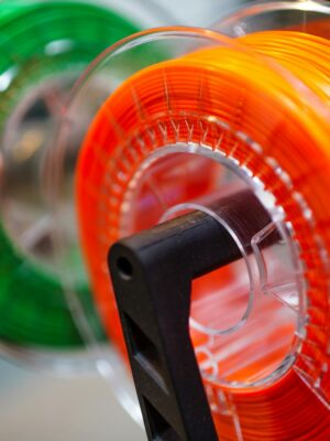 Vibrant orange and green 3D printer filament spools for innovative manufacturing uses.